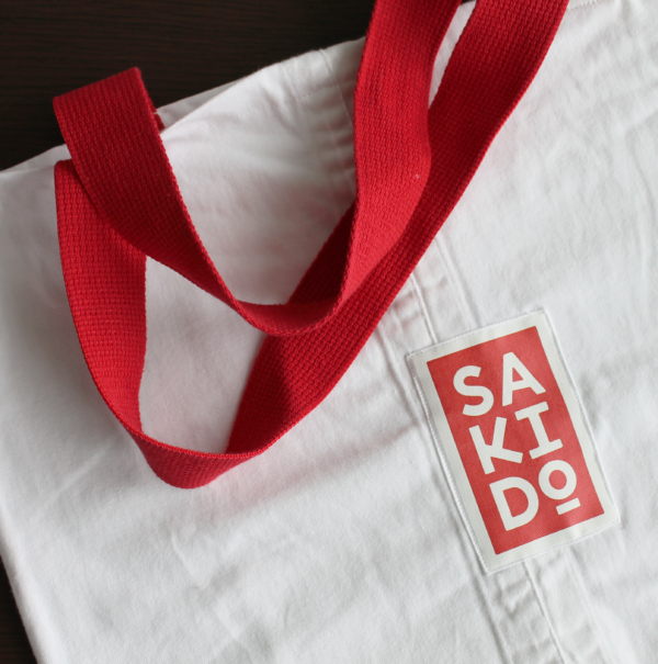 Gros plan d'un Tote bag MEIYO en toile de judogi blanche avec un logo Sakido rouge et des anses rouges.