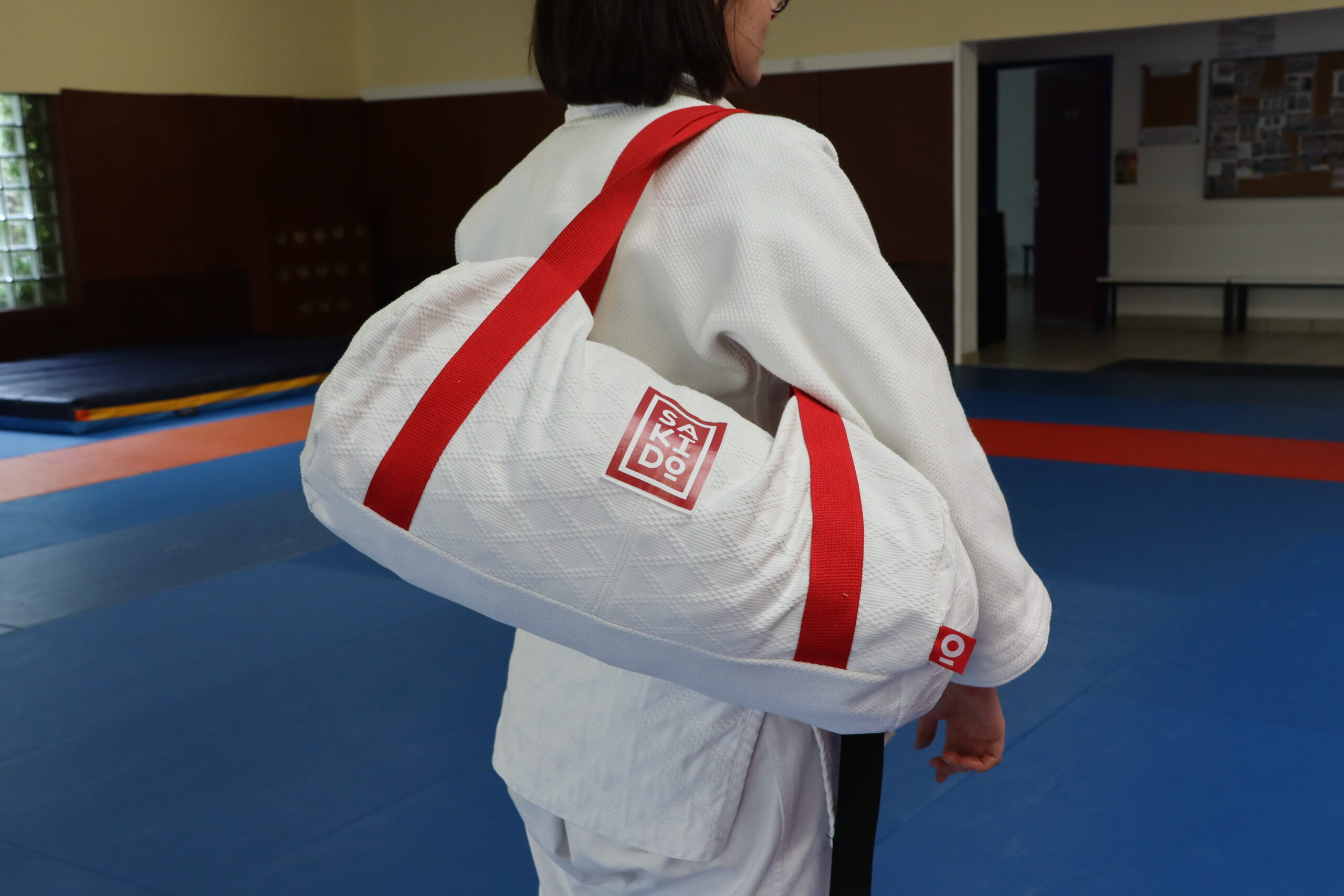 Une personne portant un judogi blanc avec un sac Sakido, vue de dos dans un dojo.